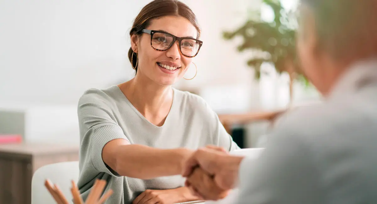 smiling-woman-shakes-man's-hand-at-desk