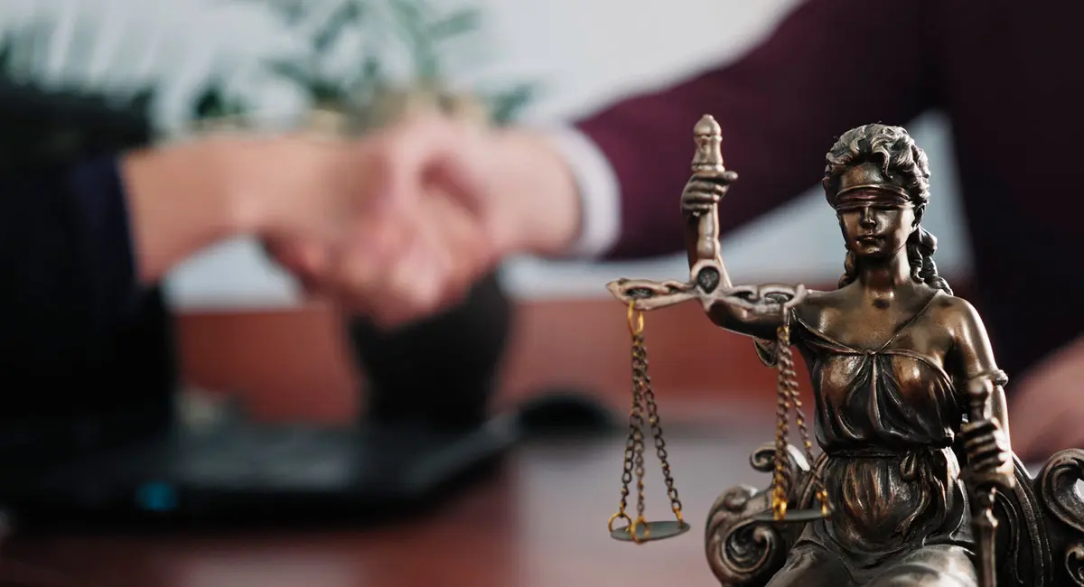 two people shaking hands with justice statue in the foreground