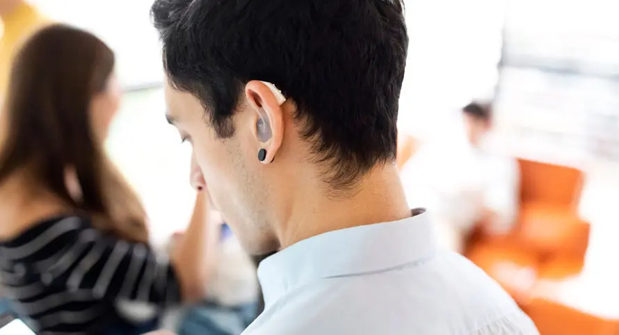 man-with-hearing-aid-in-office-looking-at-his-phone