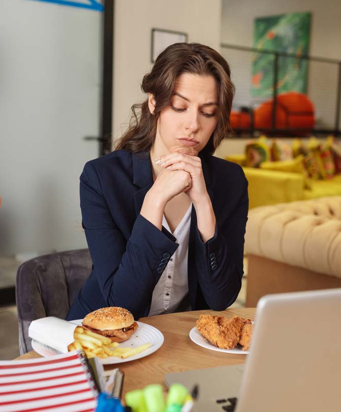 Thinking-young-woman-in-a-blue-blazer-sitting-at-a-workplace-in-the-office-and-looking-at-food-in-plates Thinking-young-woman-in-a-blue-blazer-sitting-at-a-workplace-in-the-office-and-looking-at-food-in-plates