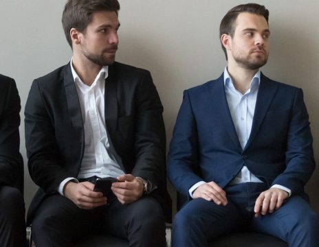 Diverse-male-applicants-looking-at-female-rival-among-men-waiting-for-job-interview
