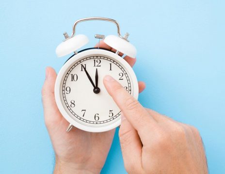 hands-holding-an-alarm-clock-against-a-light-blue-background