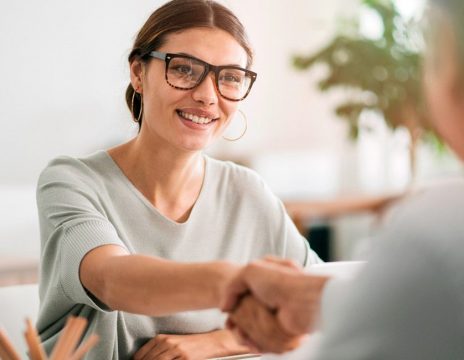 smiling woman shakes man's hand at desk
