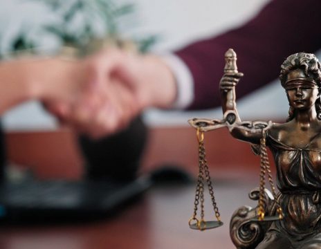 two people shaking hands with justice statue in the foreground